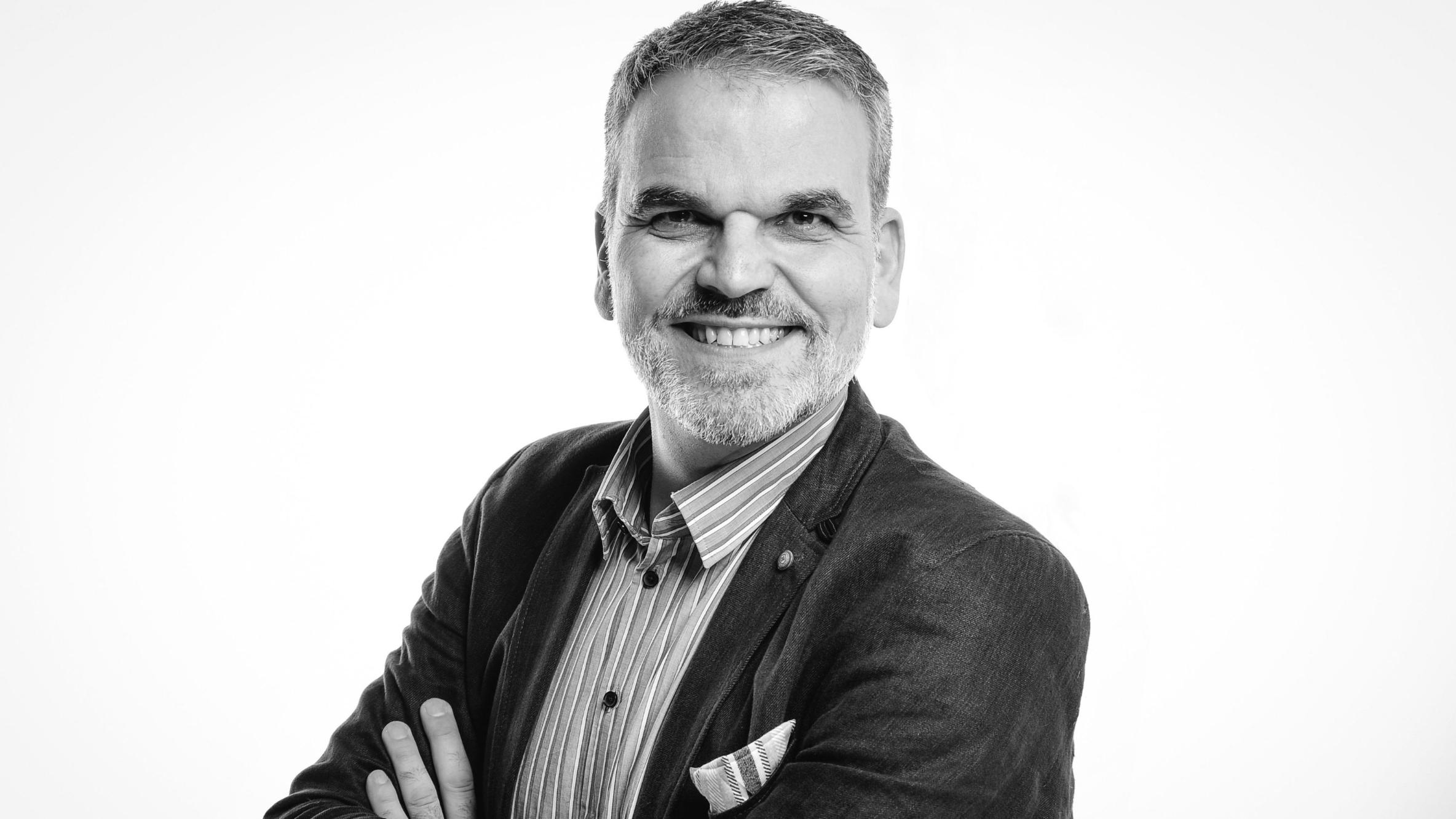 Ein Mann schaut in die Kamera und lächelt, das Foto ist in Schwarz-Weiß gehalten.