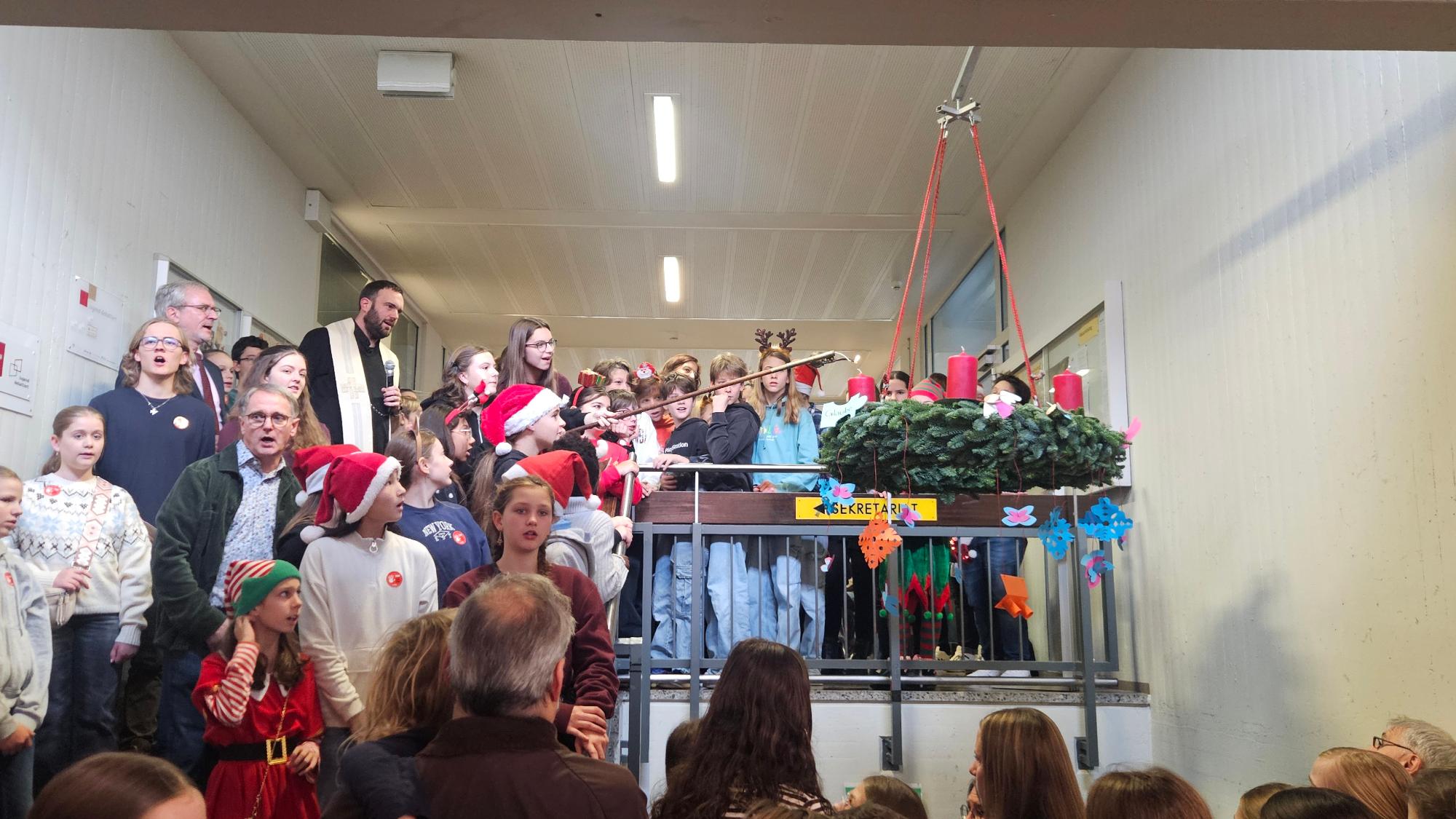 Schulpfarrer Dominic Lück segnet und entzündet gemeinsam mit der Schülervertretung die erste Kerze am Adventskranz.