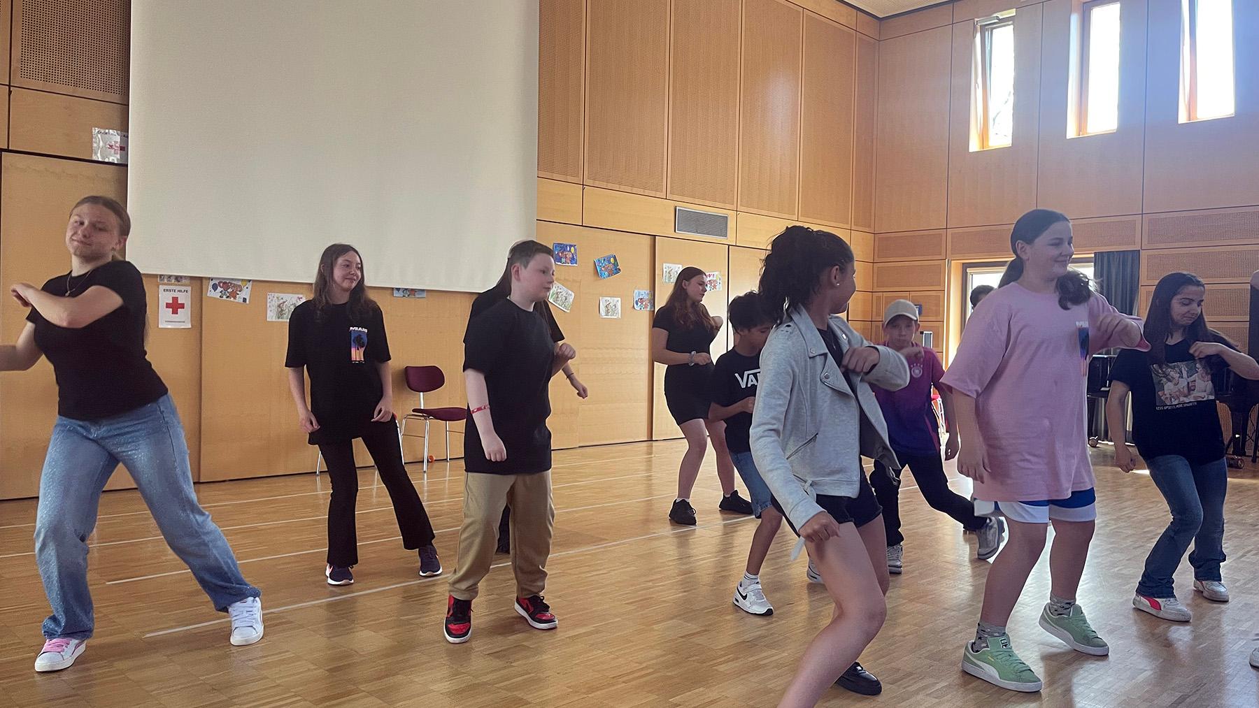 Eine Gruppe von Kindern tanzen im Rahmen einer Aufführung in einer Aula