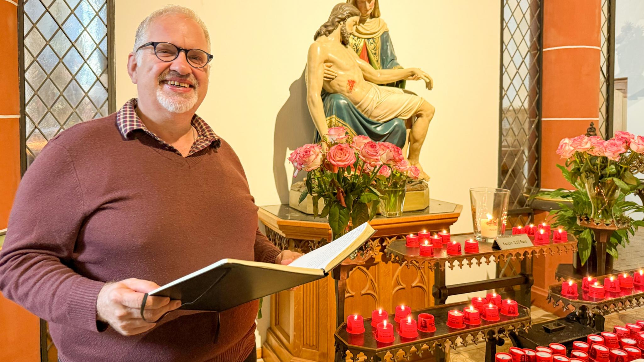 Bruder Jörg mit einem aufgeschlgenen Buch vor der Pietà in der Klosterkirche des Trierer Brüderkrankenhauses.
