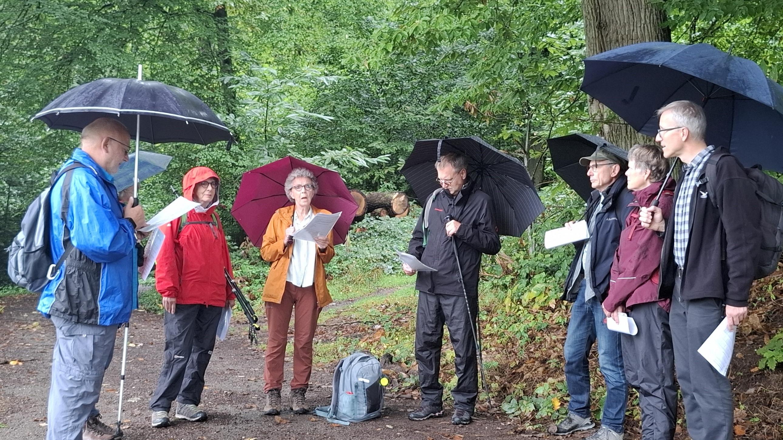 Gruppe mit Regenschirmen und Textblättern beim gemeinsamen Impuls.