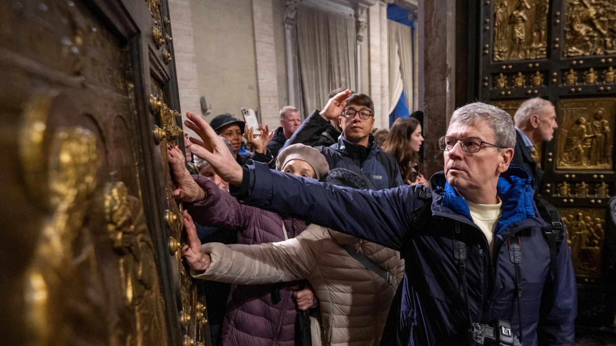 Pilger berühren  beim Durchschreiten die Heilige Pforte im Petersdom im Vatikan.