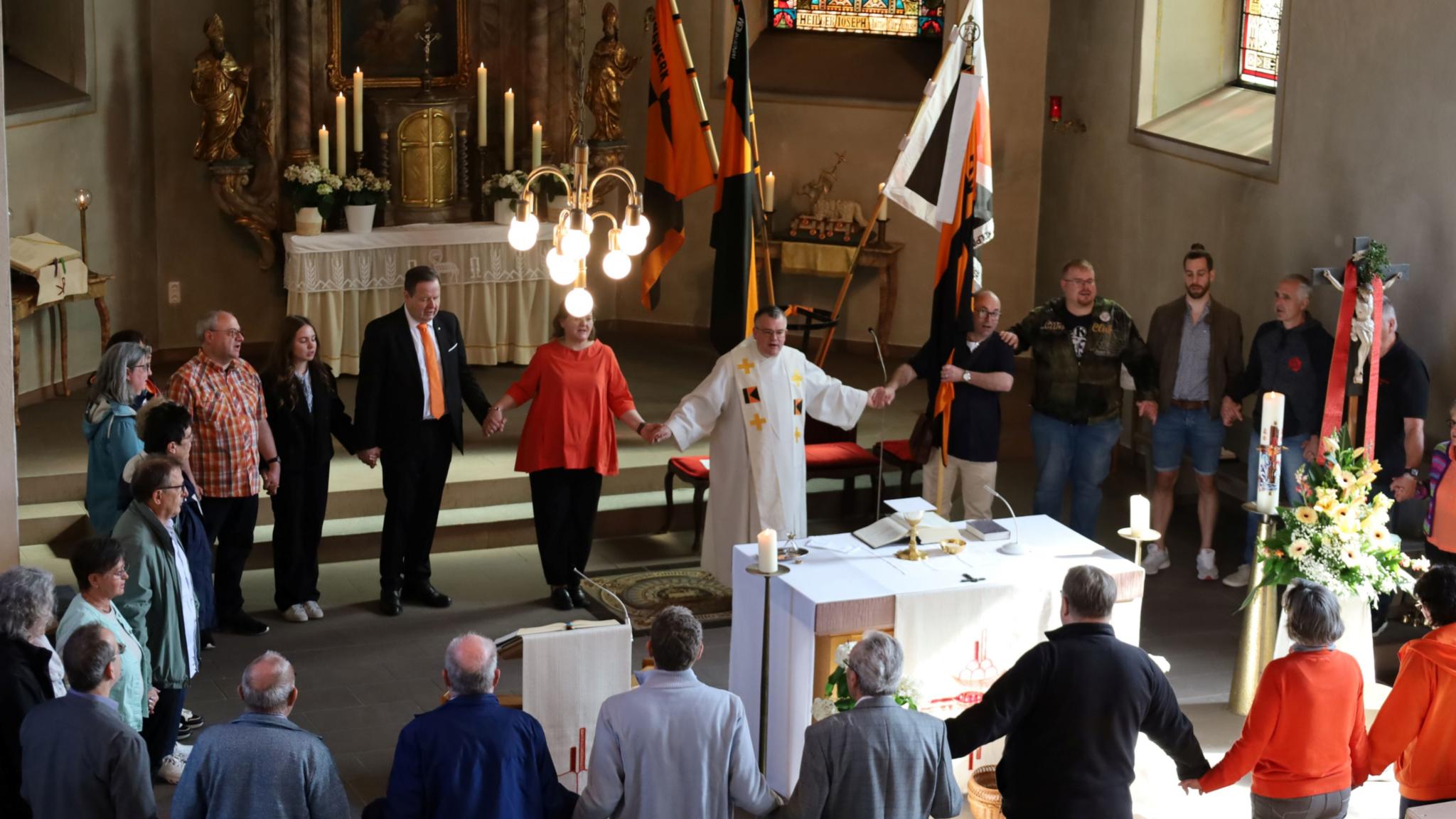 Menschen halten sich bei den Händen und bilden einen Kreis um den Altar
