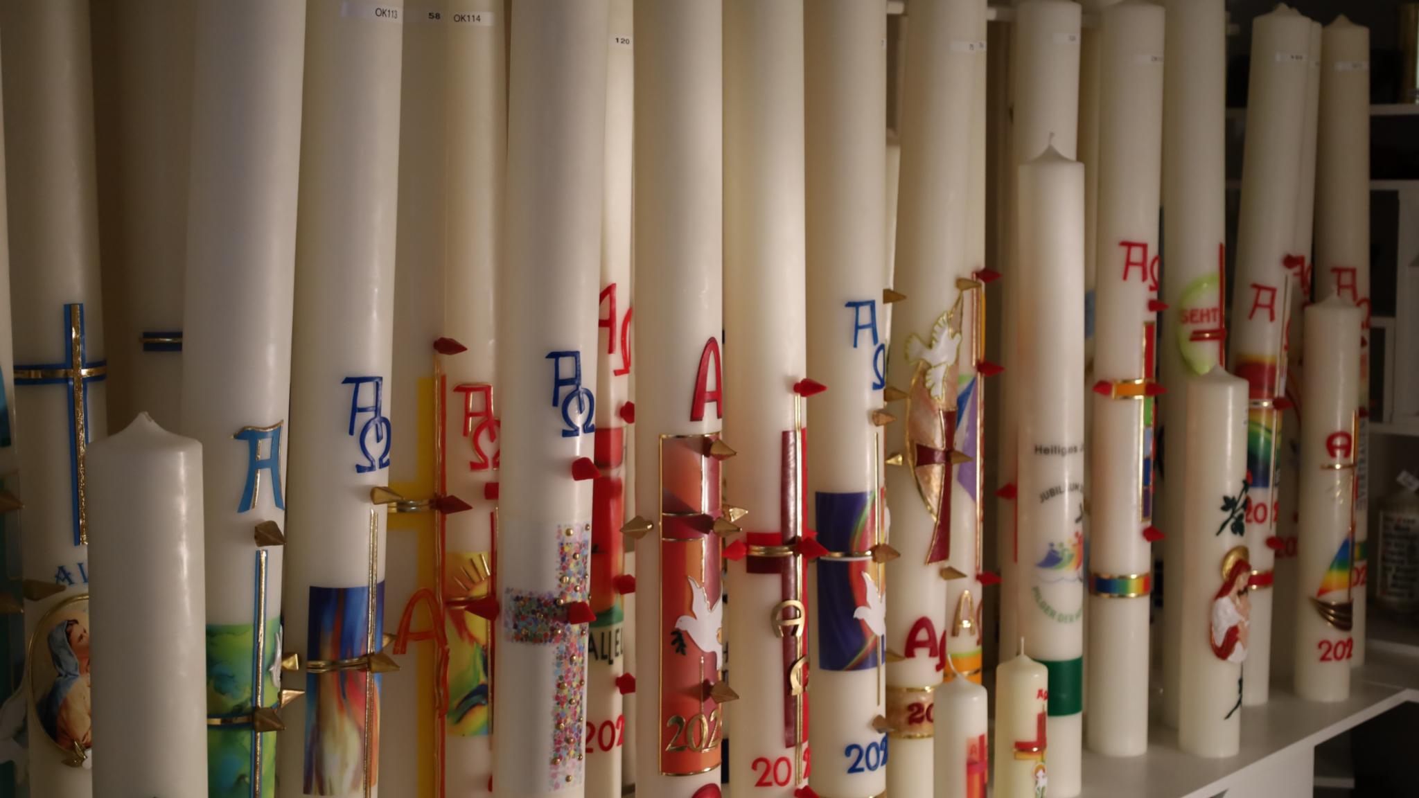 Eine Reihe hoher, bunt verzierter Kerzen mit christlichen Symbolen.