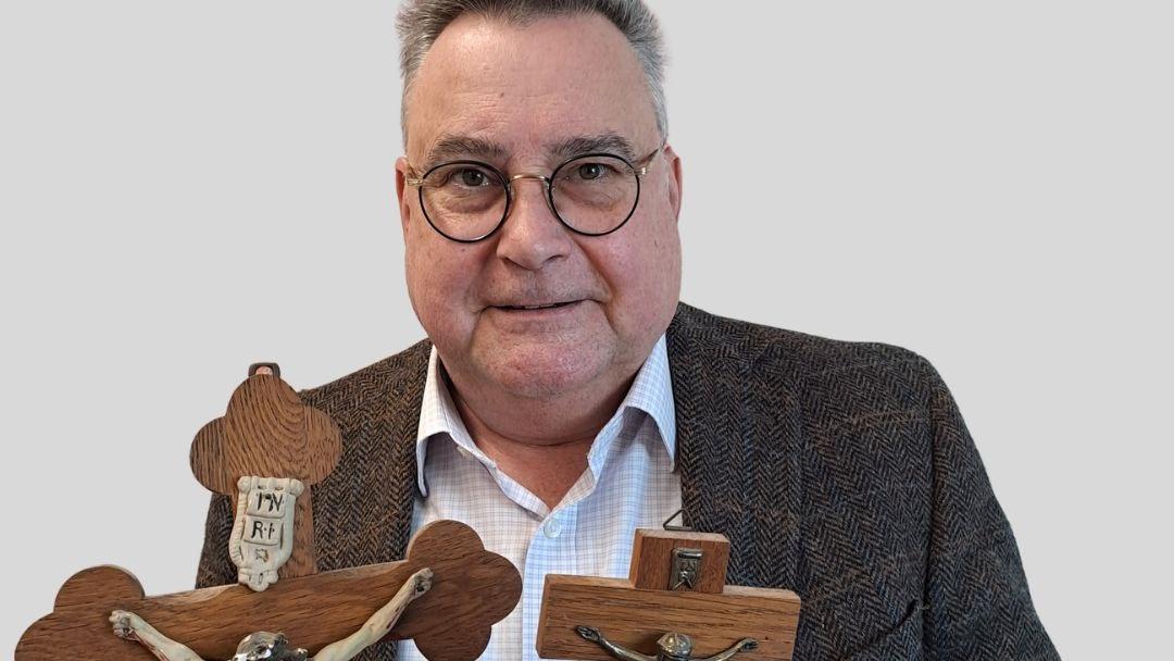 Ein Mann hat zwei alte Kreuze in der Hand und schaut in die Kamera