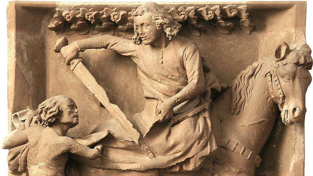 Relief aus hellem Stein: Reiter teilt seinen Mantel mit einem Bettler. (Alt-Text erstellt mit KI-Unterstützung)