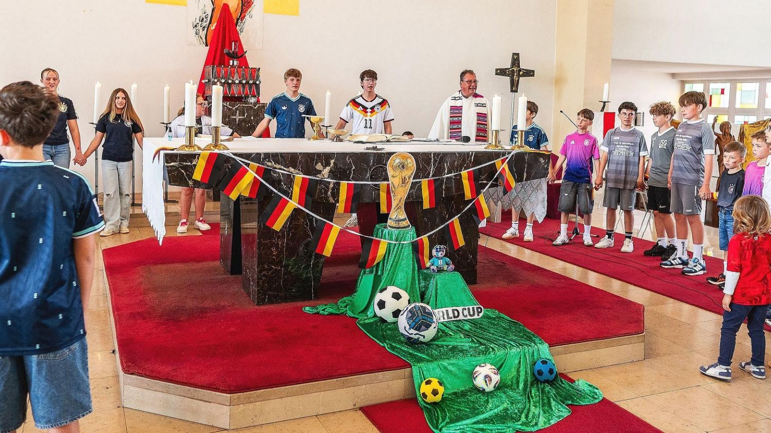Pfarrer Peter Leick stehlt gemeinsam mit Kindern im Fußball-Dress um den passend zur WM geschmückten Altar