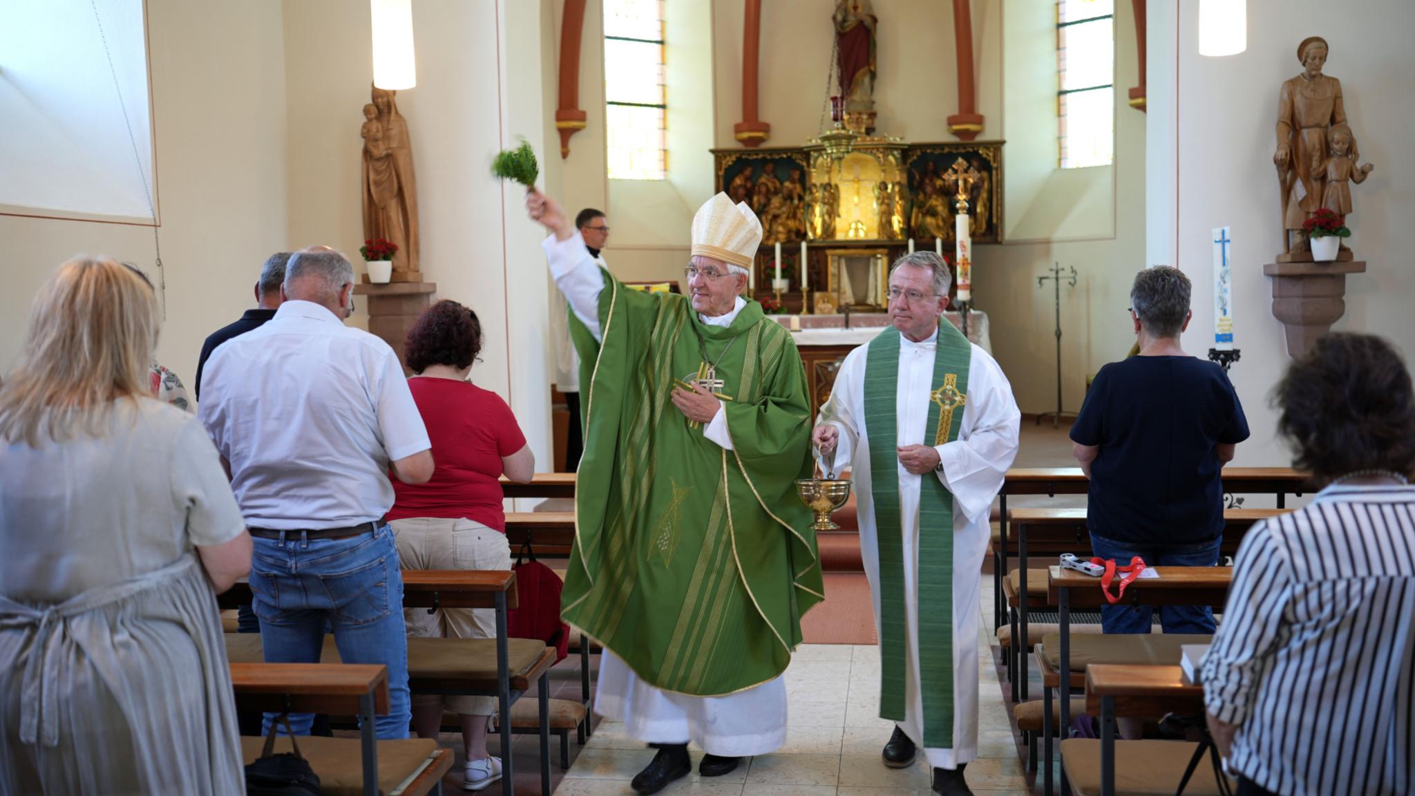 Weihbischof em. Gebert im Innenraum der Pfarrkirche; er segnet sie mit einem Palmzweig