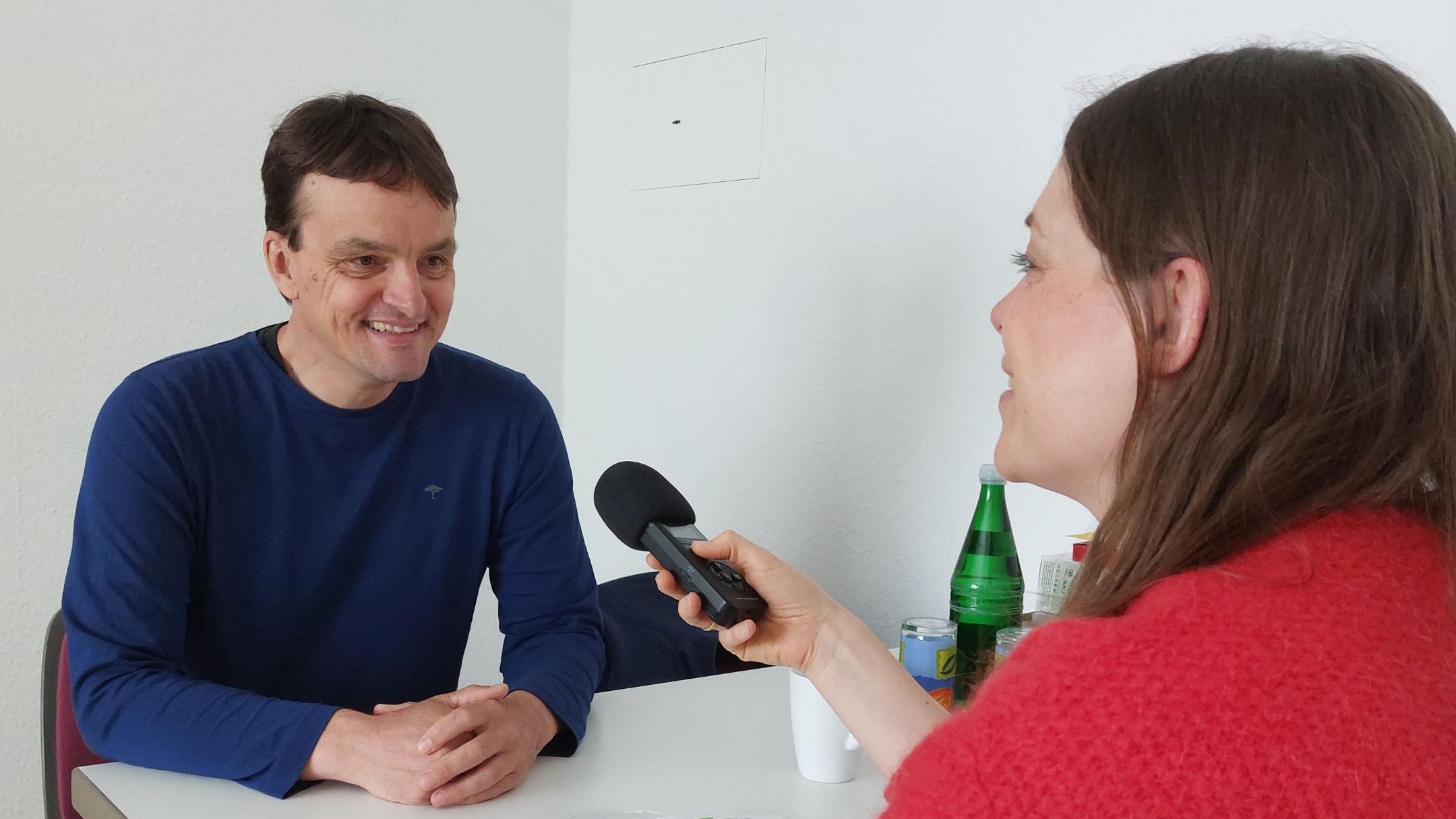 Ein Mann sitzt mit einer Frau am Tisch und sie unterhalten sich mit einem Mikrofon für die Podcastaufnahme